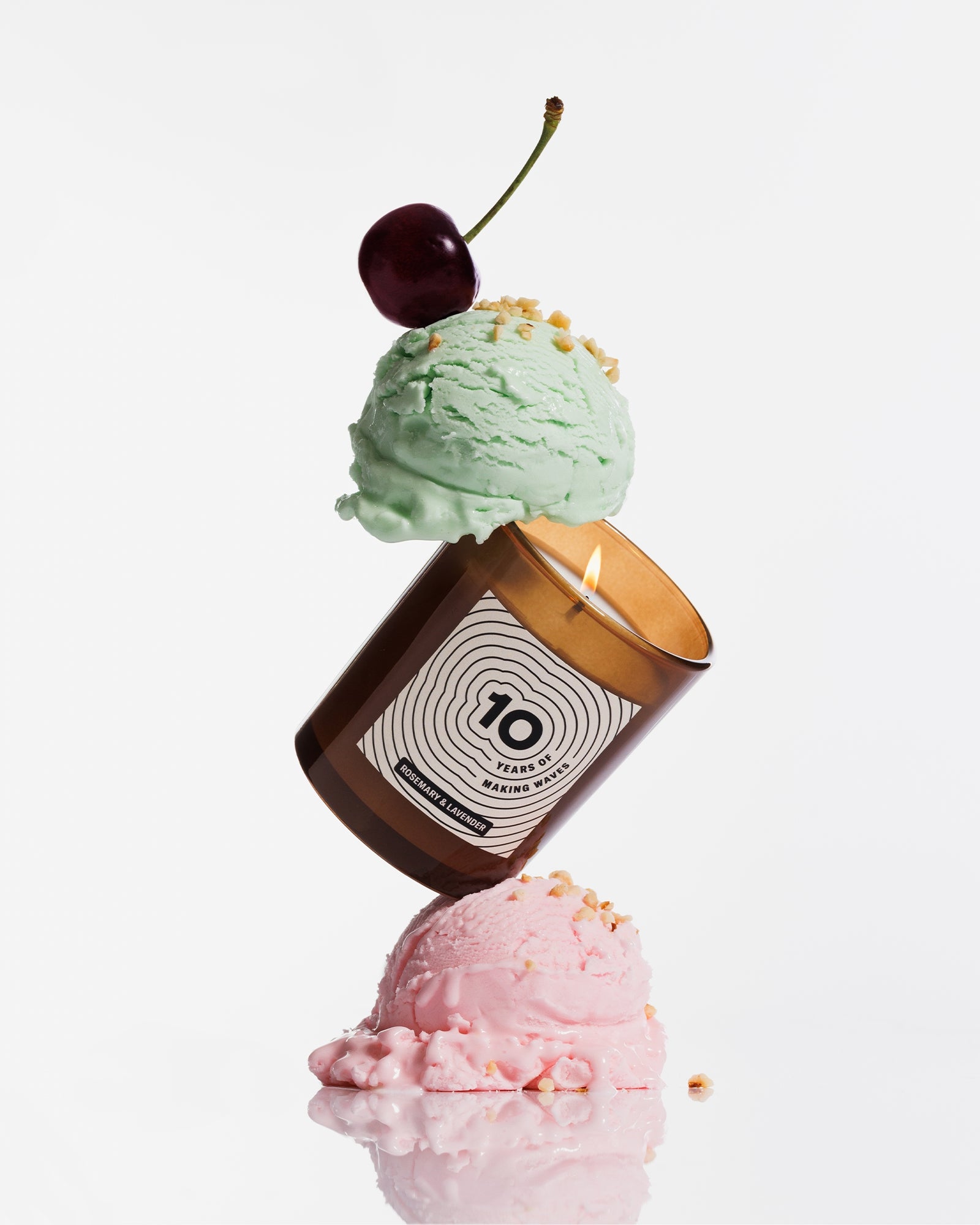 Une bougie marron équilibrée entre deux boules de glace pastel, surmontée d’une cerise.