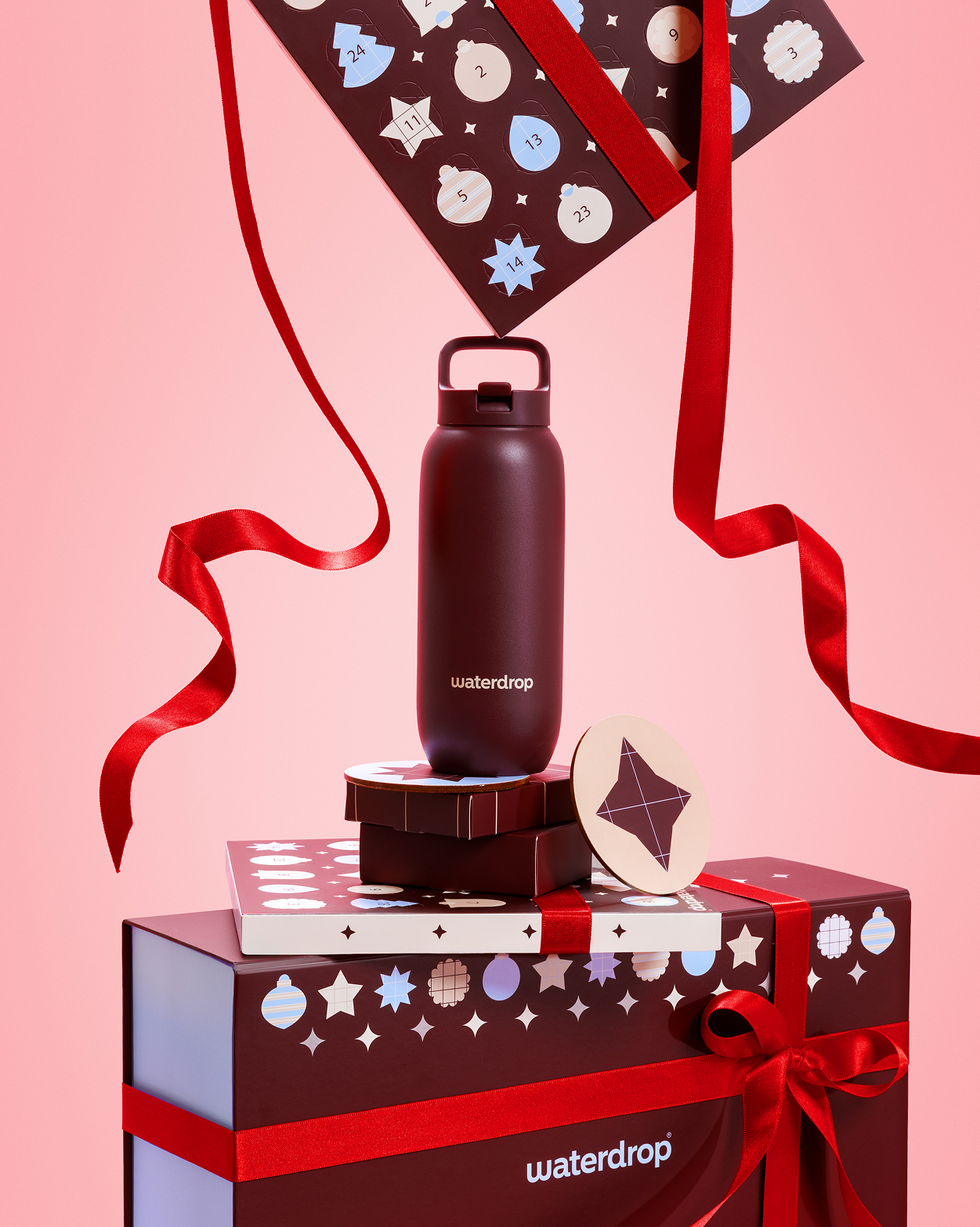 Bouteille sombre sur des boîtes cadeaux avec des rubans rouges sur fond rose.