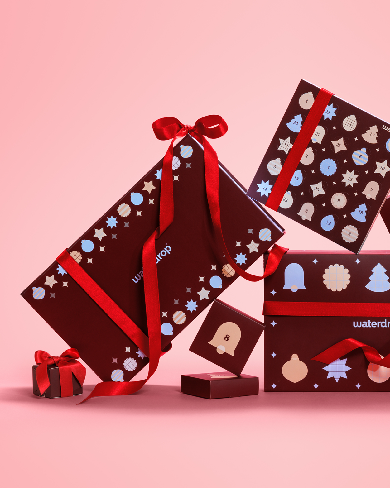 Boîtes cadeaux emballées avec des rubans rouges et des motifs festifs sur fond rose.