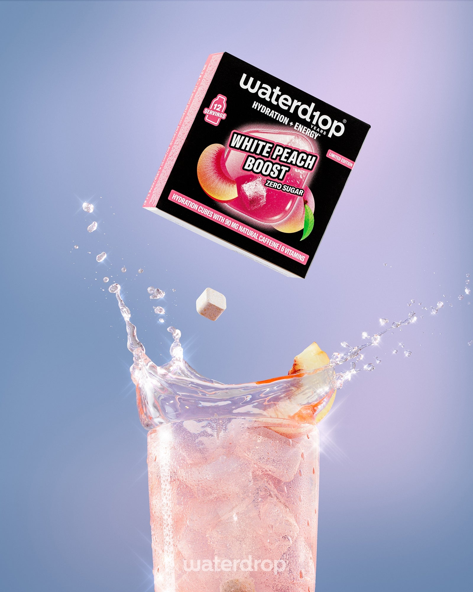 Boîte du mélange White Peach Boost au-dessus d’un verre haut contenant une boisson rosée avec des glaçons.