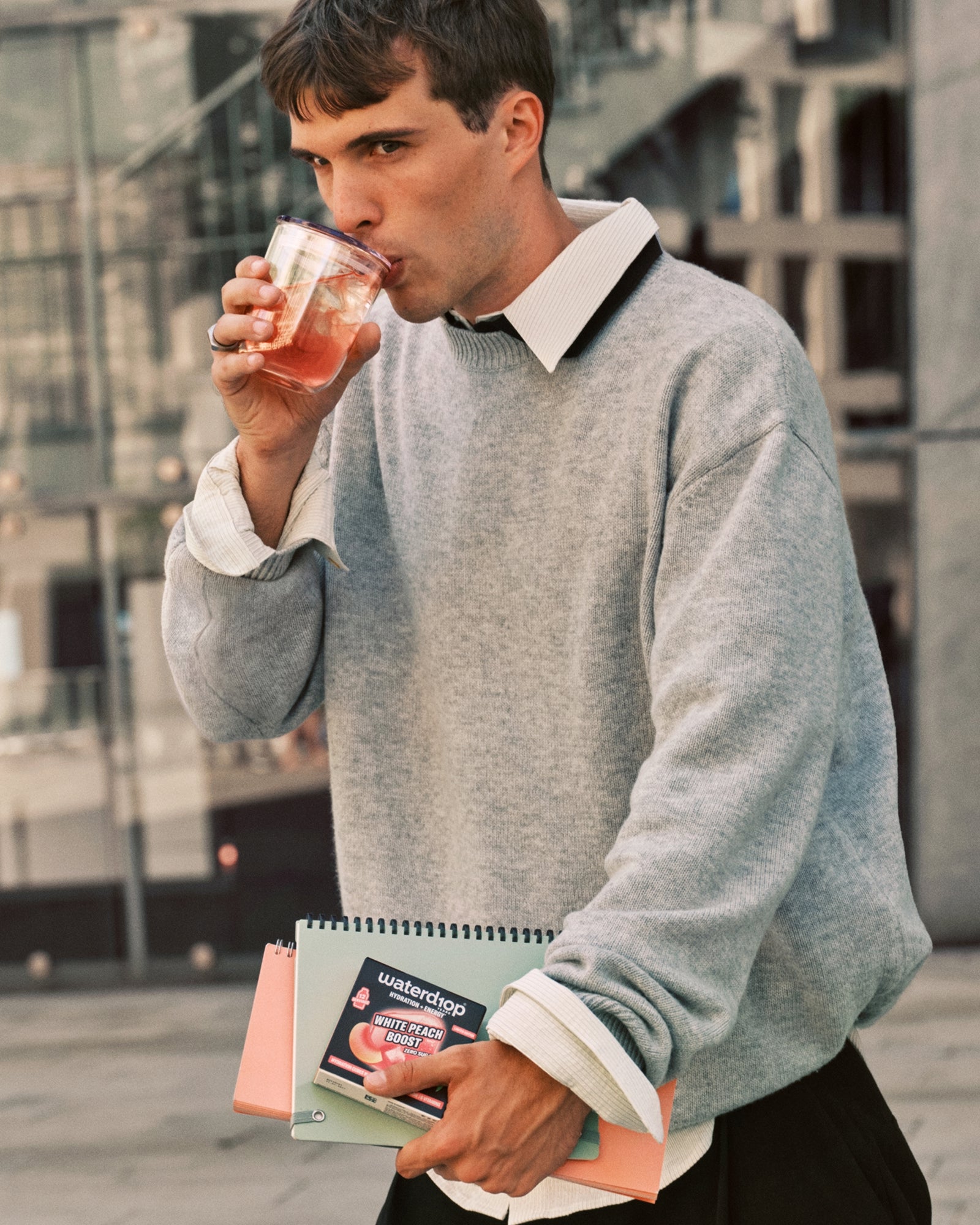 Homme en pull gris boit dans une tasse tout en portant des carnets.