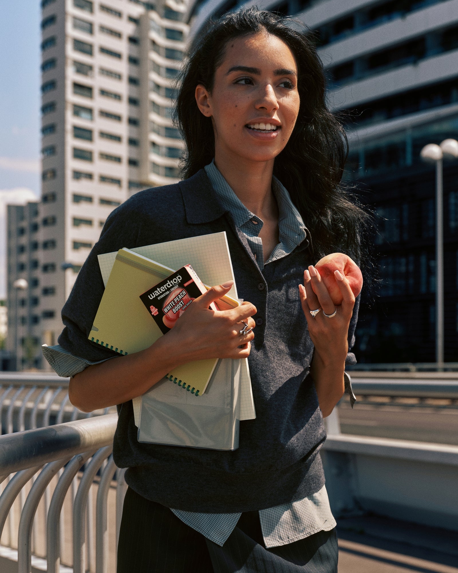 Une femme marche en plein air dans un cadre urbain, portant des cahiers et une carte.