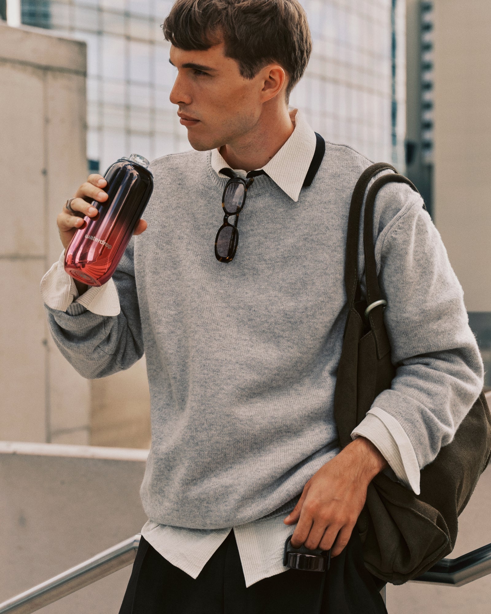 Homme jeune en sweat gris et chemise blanche avec sac à dos, buvant dans un gobelet à dégradé.