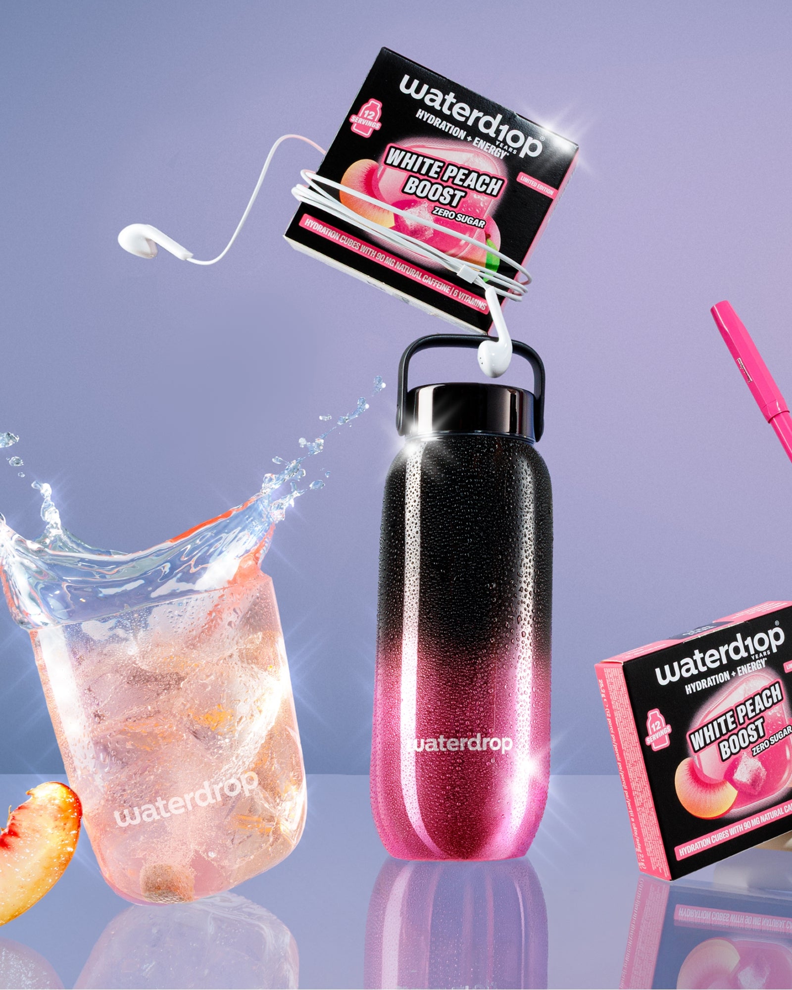 Bouteille réutilisable avec dégradé rose à noir et poignée, sachets aromatisants fixés, verre de glace avec tranche de pêche et accessoire paille rose.