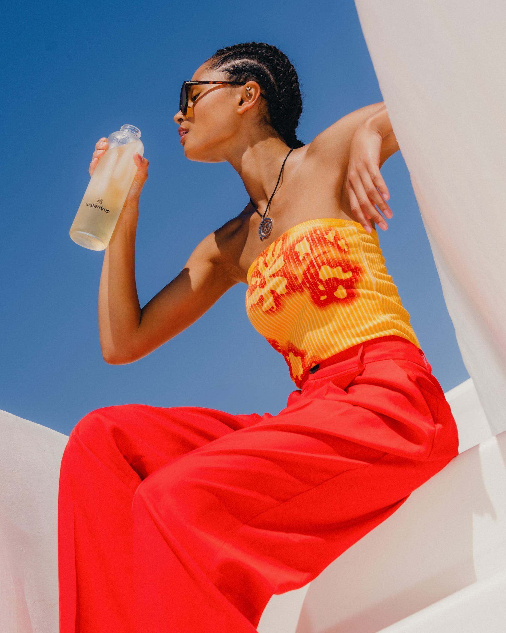 Woman drinking THÉ GLACÉ PÊCHE from bottle outdoors.